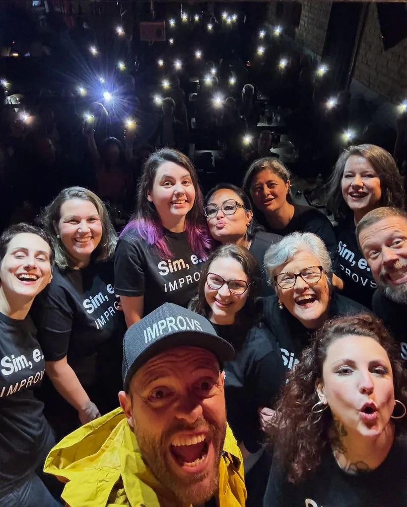 Selfie da turma no palco do São Léo Comedy com a plateia acendendo as lanternas dos celulares ao fundo